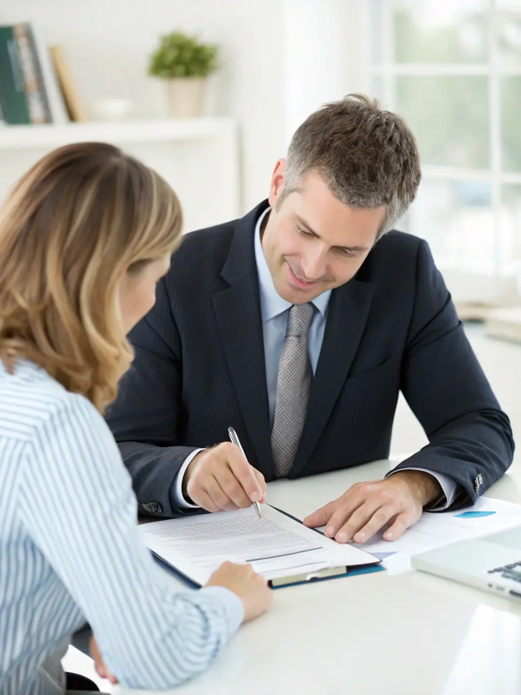 A professional Indian financial advisor in a modern office, explaining insurance options to a young Indian couple, with charts and graphs visible in the background.